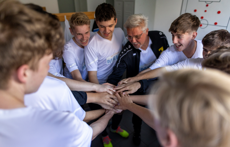 Eine Fußballmannschaft schwört sich vor dem Spiel in der Kabine ein, indem sie ihre Hände übereinander legen.